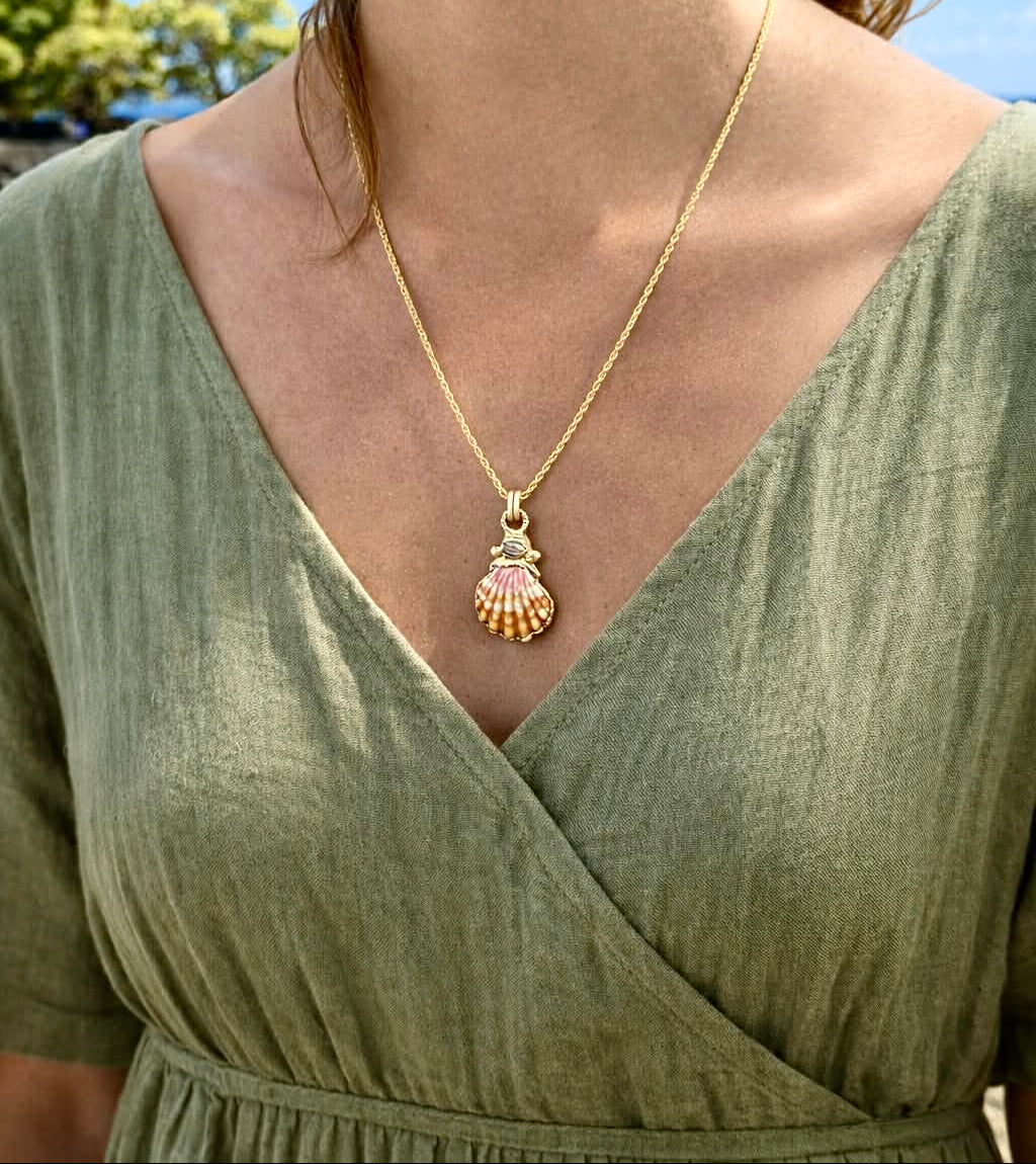 Woman wearing a gold necklace with a shell pendant outdoors