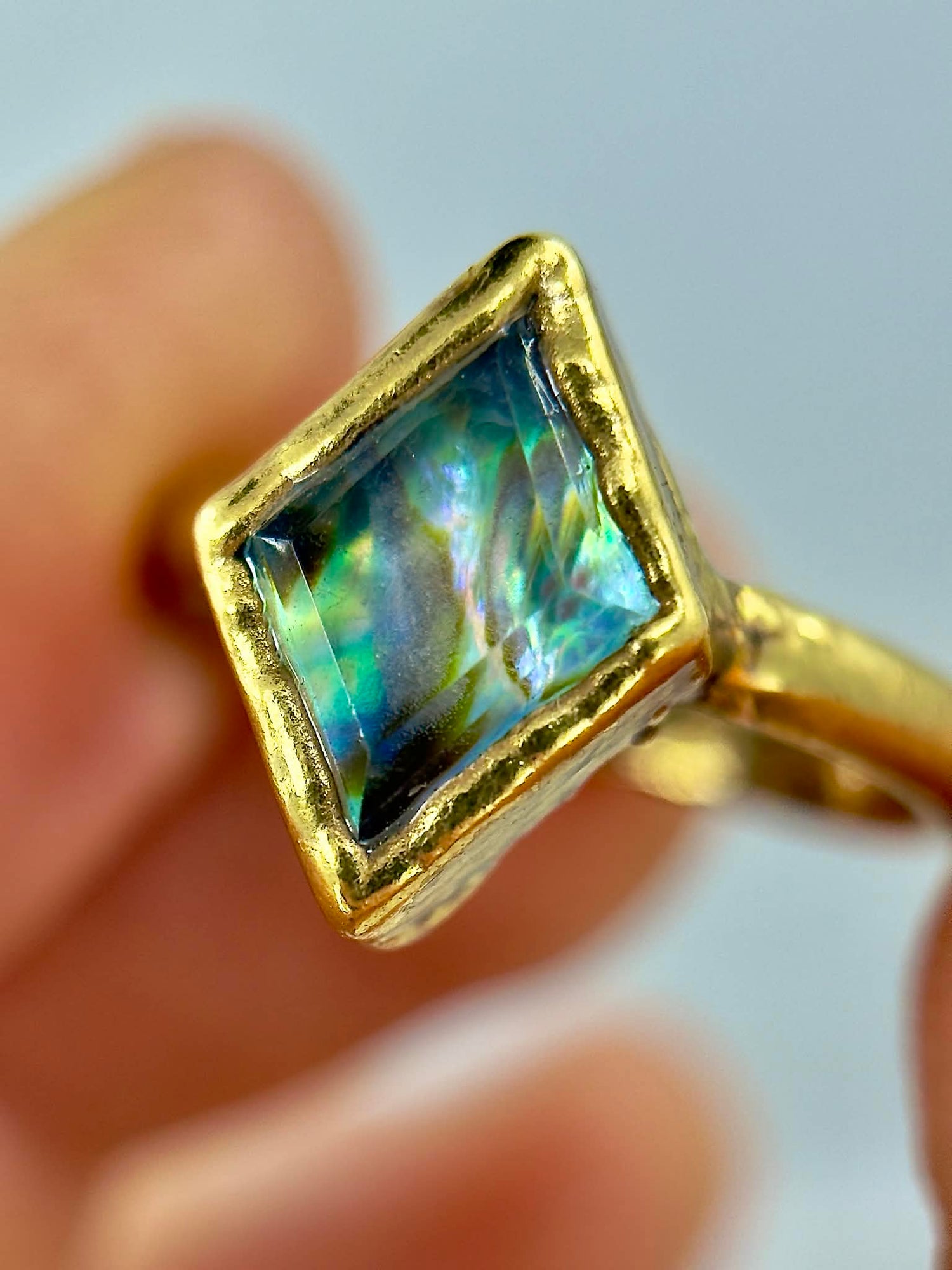 Gold ring with a square-cut gemstone held in hand against a neutral background