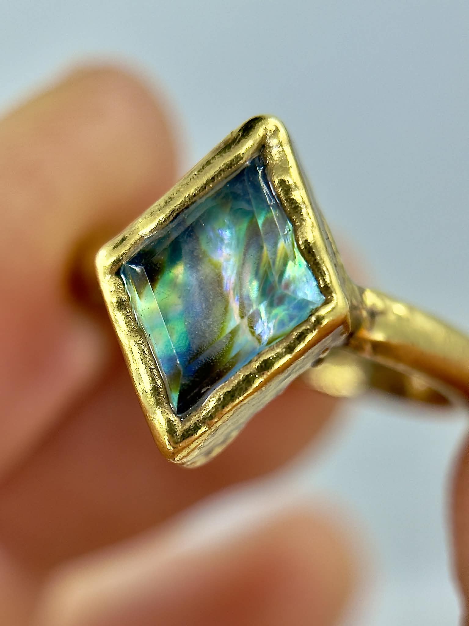 Gold ring with a square-cut gemstone held in hand against a neutral background