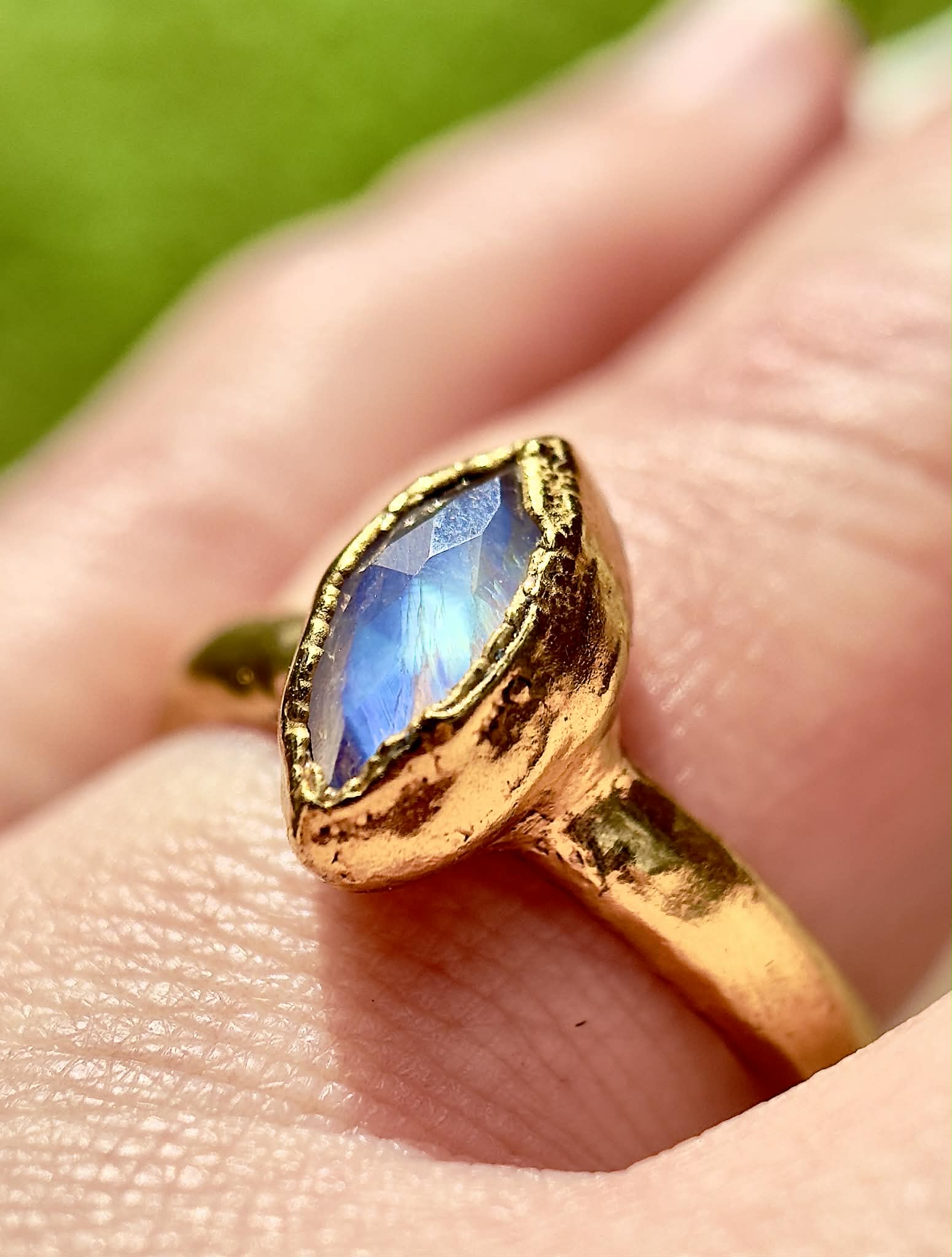 Gold ring with a blue gemstone held on a hand against a green background