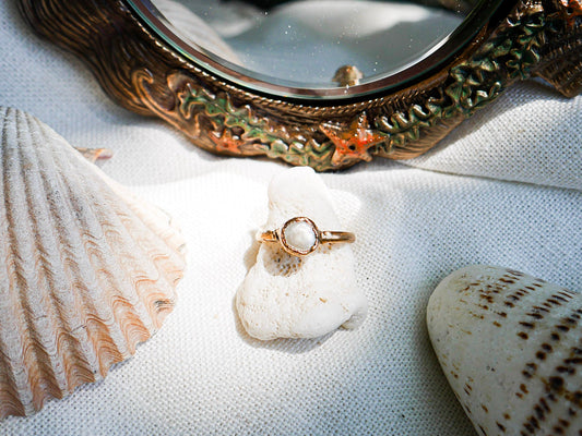 Gold ring on a white shell with seashells and a decorative mirror in the background