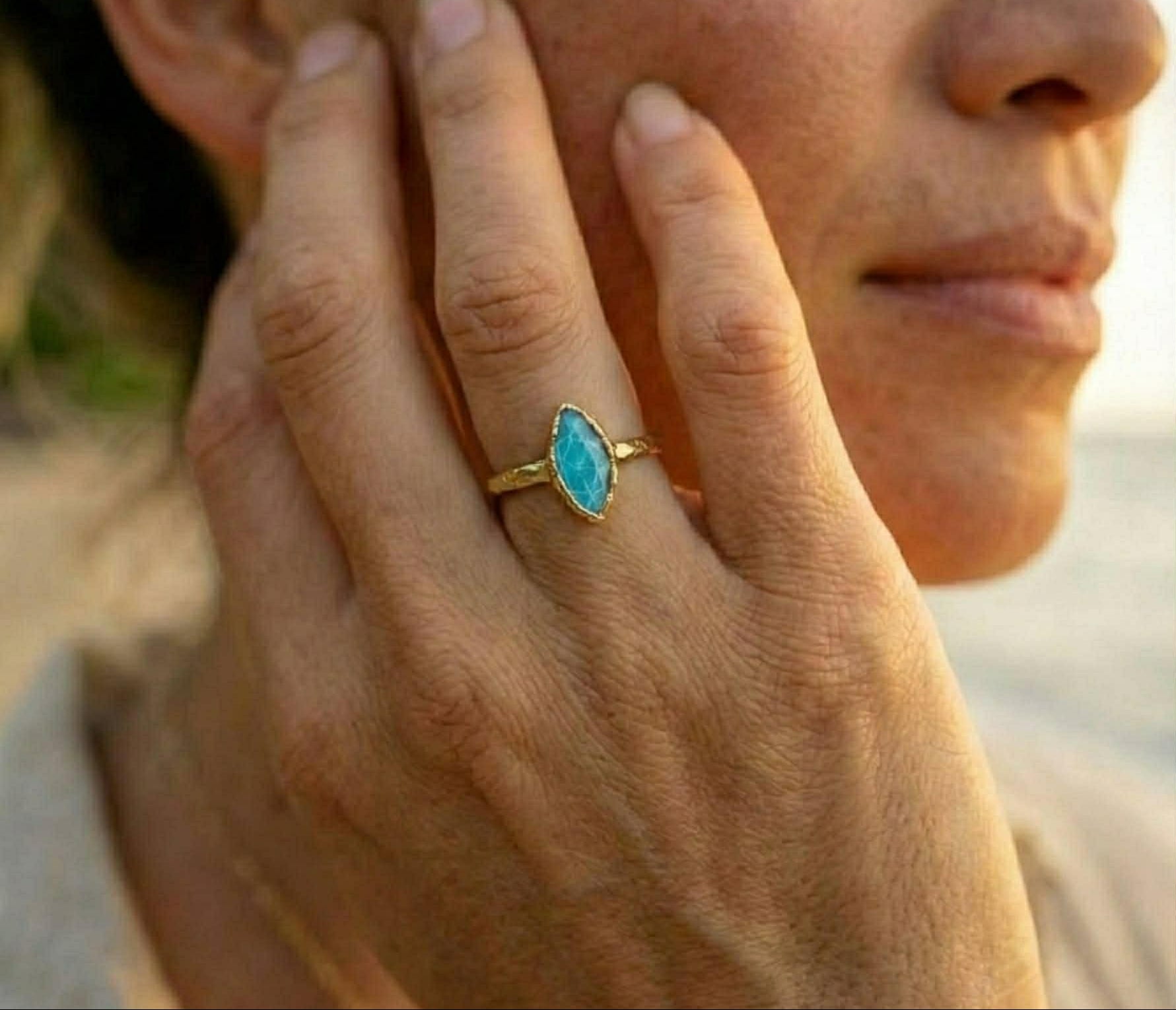 Close-up of a hand wearing a turquoise ring with a blurred background